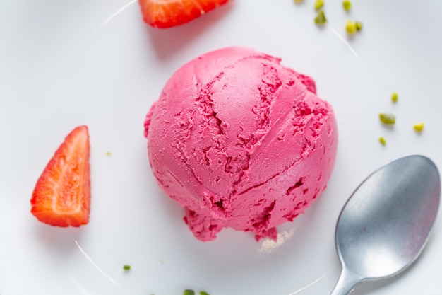 Boule de crème glacée à la fraise fruitée servie sur assiette avec des fruits et des pistaches. Vue de dessus.