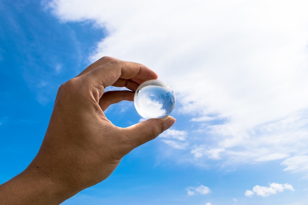 Boule de cristal ou boule de terre de verre. Sphère transparente à la main avec fond de ciel clair.