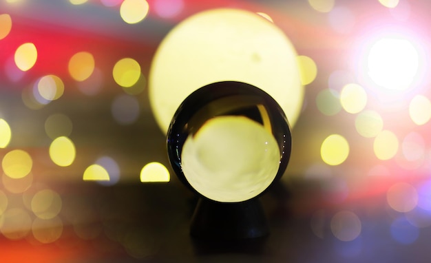 Boule de cristal sur la table avec des lumières bokeh derrière Boule de verre avec concept de prédiction de lumière bokeh coloré