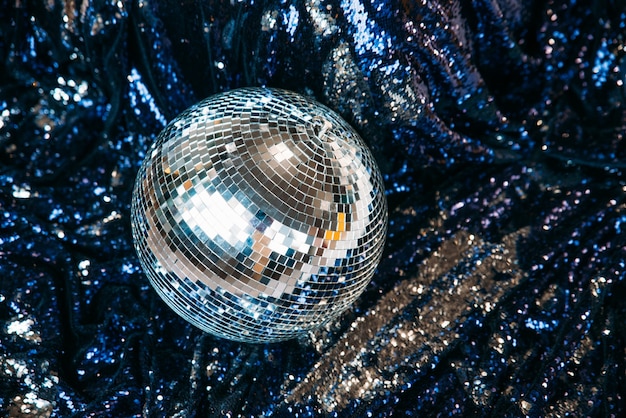 Une boule à facettes disco se trouve sur un textile bleu avec des paillettes