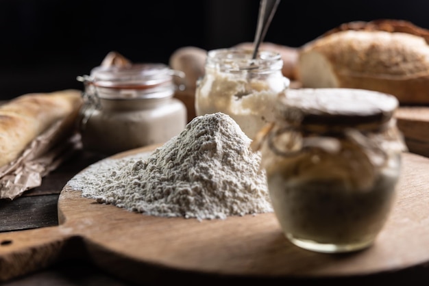 Une boule de farine lisse et autour d'elle des bocaux avec de la levure et du pain frais