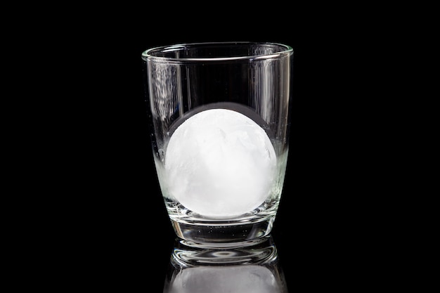 Boule de glace à l'intérieur du verre à cocktail sur une table noire réfléchissante.