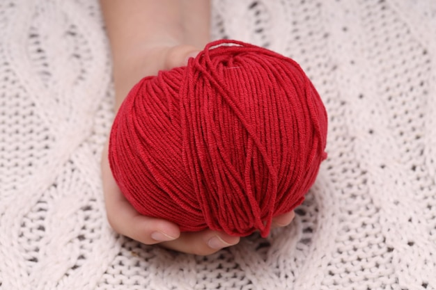 Boule de laine rouge dans les mains sur le fond d'une nappe tricotée blanche Photo de haute qualité