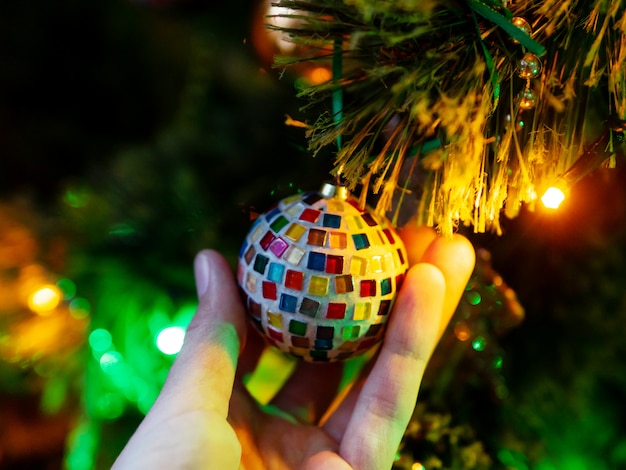 Boule de mosaïque fabriquée à la main sur l'arbre de Noël. Ampoules colorées et décorations sur le sapin traditionnel pour la célébration du nouvel an.