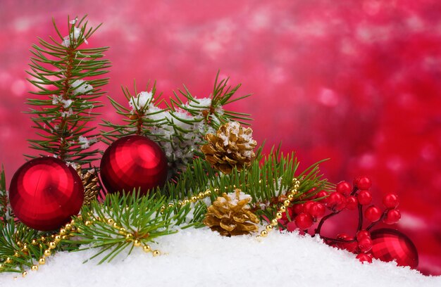 Boule de Noël et arbre vert dans la neige sur rouge