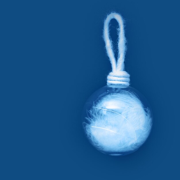 Boule de Noël avec des plumes blanches sur fond de papier bleu classique. Jouet d'hiver de vacances traditionnel suspendu. Concept de Noël minimal.