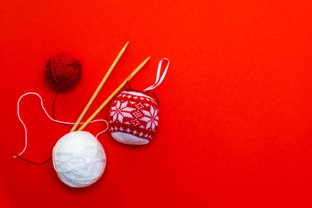 Boule de Noël tricotée et pelotes de laine avec des aiguilles à tricoter sur fond rouge. Carte de Noël, travaux d'aiguille. photo horizontale.