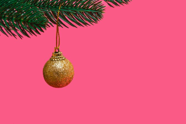 Boule d'or festive sur une branche d'un arbre de Noël isolé sur fond rose avec espace de copie