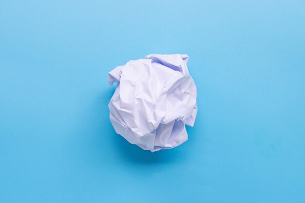 Boule de papier froissé sur table bleue.