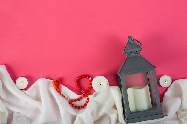 Boule de prière rouge et bougeoir avec une bougie allumée sur un drap blanc sur fond rouge