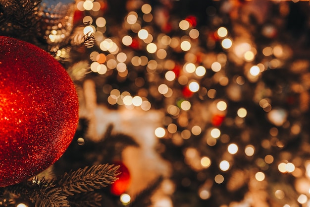 Boule rouge de jouet de Noël accrochée à l'arbre de Noël avec des lumières de bokeh festives dorées sur fond