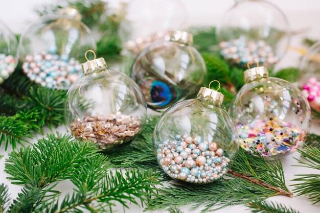 Boule transparente en verre de Noël avec des confettis scintillants colorés et une branche de sapin et de pin. Notion de vacances.