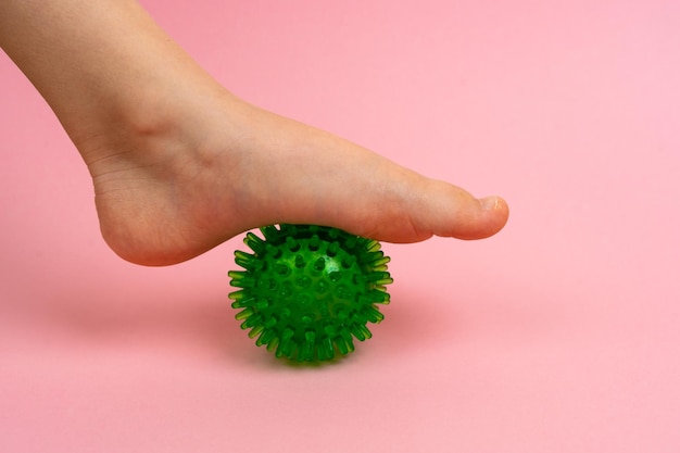 Boule verte d'aiguille pour le massage et la thérapie physique sur un fond rose avec un pied d'enfant le