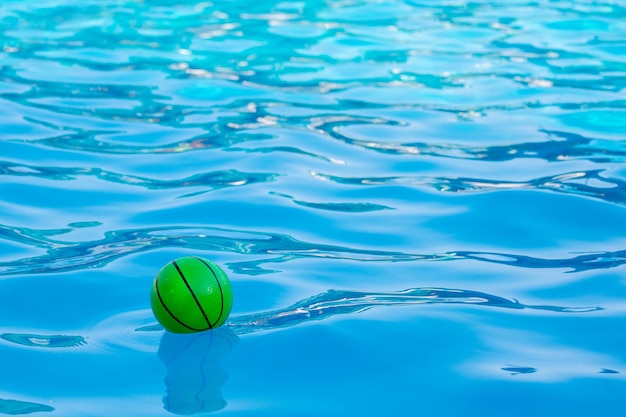 Boule verte dans l'eau claire de la piscine. Vacances d'été en mer_