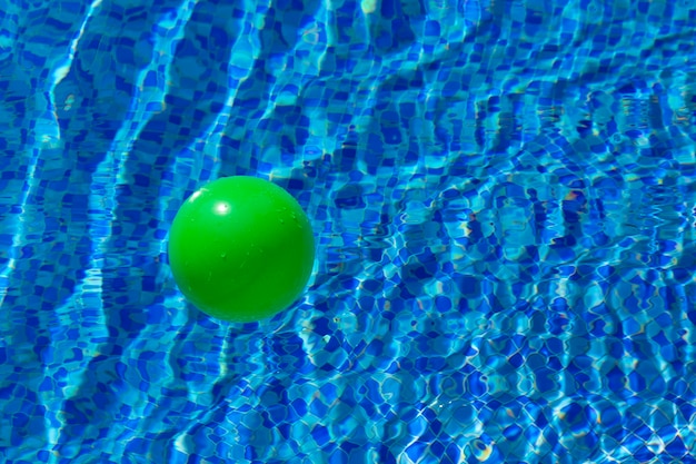 Boule verte ronde à la surface de l'eau dans une piscine avec de l'eau bleue et des vagues Le concept de sécurité des enfants près de l'eau