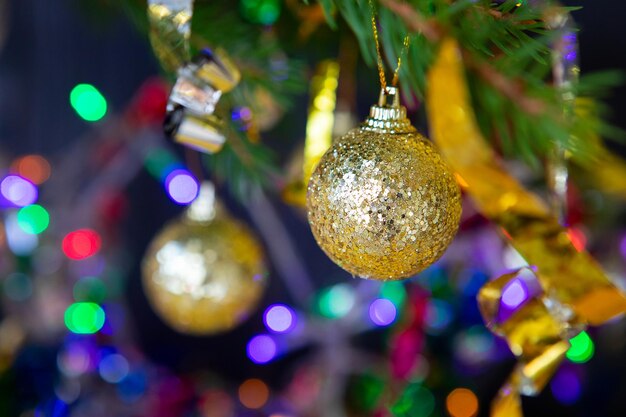 Photo des boules d'arbre de noël dorées sur une branche en gros plan sur un fond sombre à l'arrière-plan sont les lumières de guirlandes et de serpentines