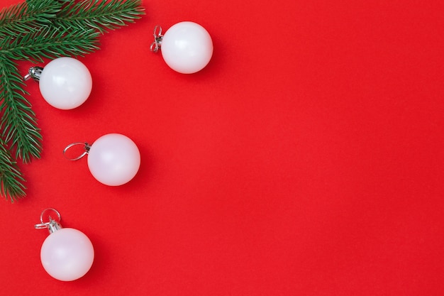 Boules blanches de Noël et brindilles de sapin sur papier rouge