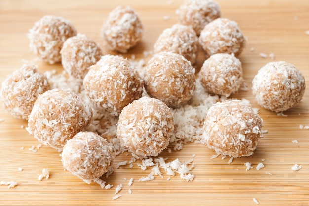 Boules de bonbons sucrés faits maison en copeaux de noix de coco sur bois de bambou naturel. Concept de mode de vie sain. Fermer. Flou sélectif. Espace de copie de texte.