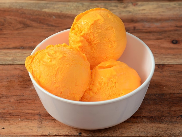 Boules de crème glacée à la mangue servies dans un bol blanc sur une table en bois rustique mise au point sélective