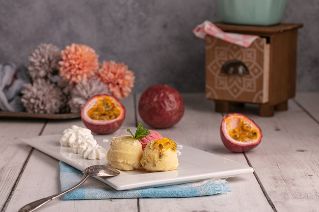 Boules de crème glacée passion, vanille et fraise sur une plaque blanche sur une table en bois