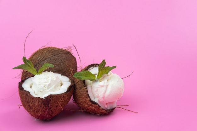 Boules de crème glacée à la vanille dans des moitiés de noix de coco fraîches décorées de feuilles de menthe sur fond rose