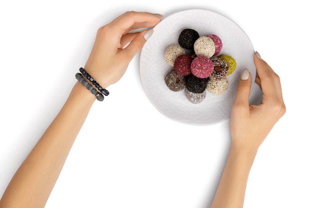 Boules d'énergie de bonbons végétaliens sur une assiette avec des mains de femme blanches isolées