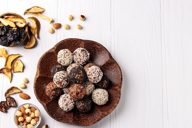 Boules d'énergie de noix, flocons d'avoine et fruits secs avec graines de lin et de sésame, flocons de noix de coco sur une plaque en bois de noix de coco sur fond blanc, orientation horizontale, vue de dessus