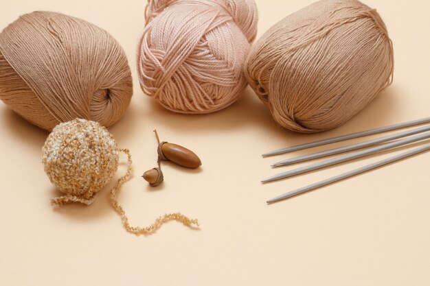 Boules de fil à tricoter, aiguilles à tricoter en métal et gland sur fond beige. Notion de tricot.