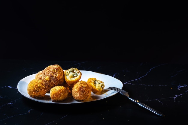 Boules de fromage à l'ail et à l'aneth à l'intérieur pour une collation dans une assiette sur fond noir.