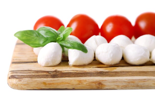 Boules de fromage mozzarella savoureuses au basilic et tomates rouges, sur une planche à découper, sur blanc