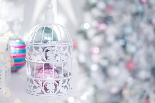 Boules de jouets de Noël argent bleu rose en cage ajourée blanche sur fond de lumières de Noël.