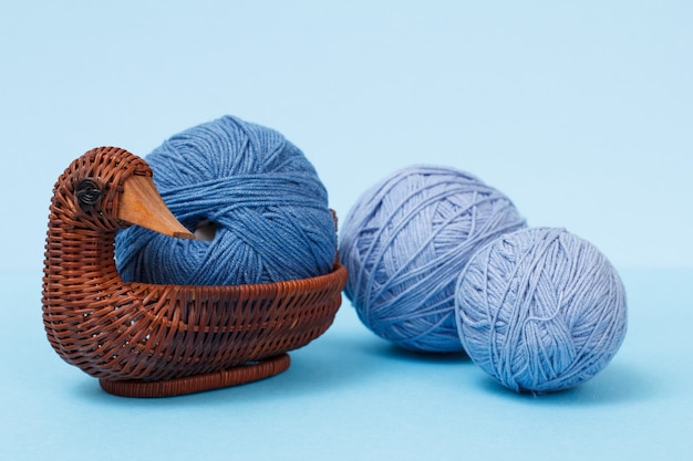 Boules de laine à tricoter et panier en osier sur fond bleu. Notion de tricot.