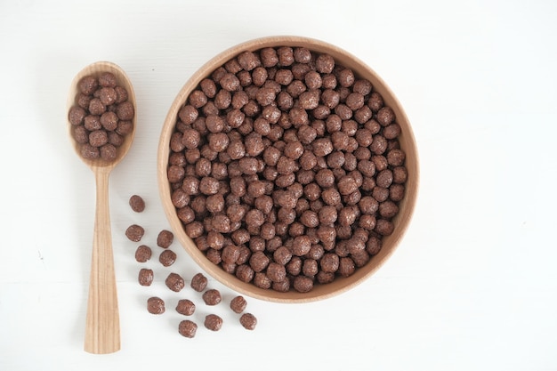 Boules de maïs au chocolat dans un bol et une cuillère en bois éparpillés sur un fond blanc