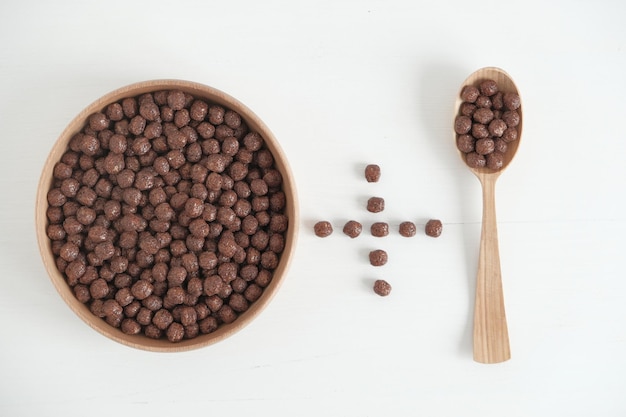 Boules de maïs au chocolat dans un bol et une cuillère en bois éparpillés sur un fond blanc