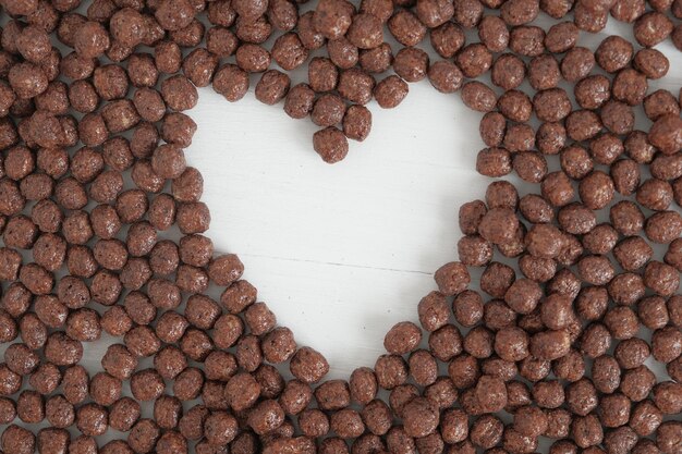 Boules de maïs au chocolat éparpillées en forme de coeur sur fond blanc