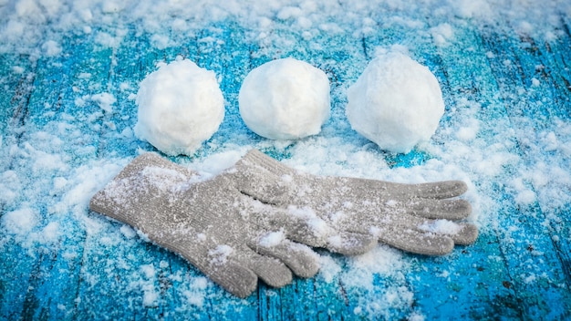 Boules de neige et mitaines sur une surface en bois peinte en bleu recouverte de neige