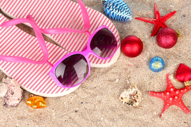 Boules de Noël, coquillages et accessoires de plage sur le sable, gros plan