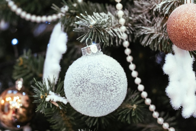 Boules de Noël or et blanc avec des étincelles sur un gros plan d'arbre de Noël enneigé