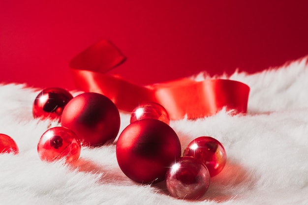 Boules de Noël rouges sur une couverture de fourrure avec un ruban rouge sur fond rouge