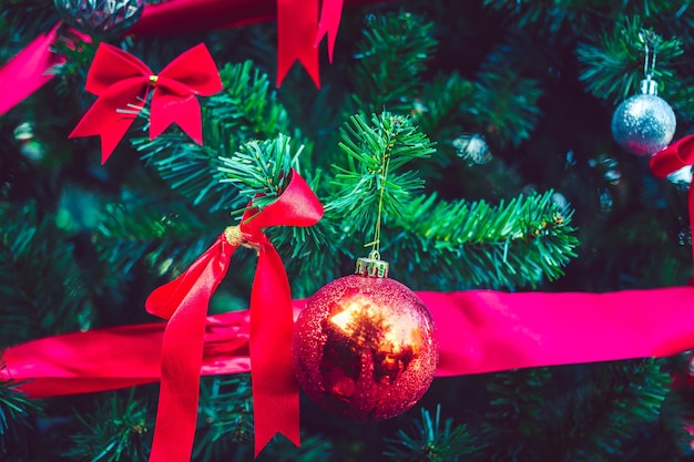 Des boules de Noël rouges et un ruban arc rouge ornent le sapin de Noël et le bokeh