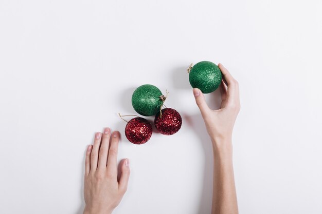 Boules de Noël rouges et vertes et mains féminines sur fond blanc