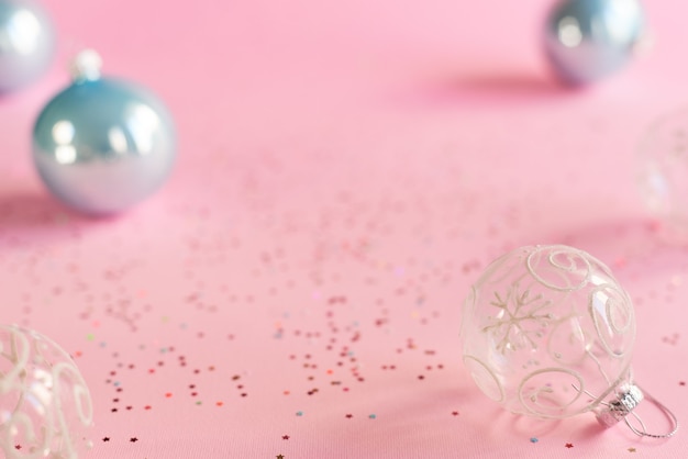 Boules de Noël transparentes et boules bleues sur fond rose avec des confettis colorés en forme d'étoile