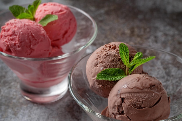 Boules roses de crème glacée à la fraise et au chocolat dans une tasse contre une table en pierre grise