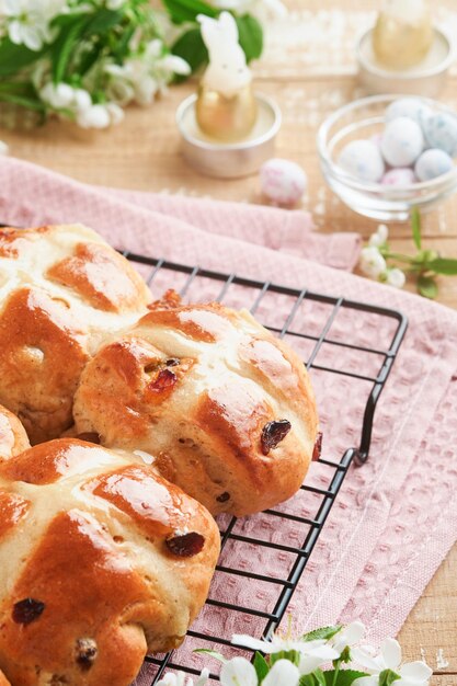 Boulets de croix chauds de Pâques Traits traditionnels de Pâque Boulettes de croix avec des raisins secs, du beurre, du chocolat, des œufs de bonbons avec des fleurs de cerises ou de pommes en fleurs sur des arrière-plans rustiques en bois clair.