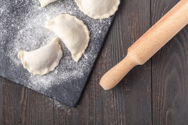 Boulettes crues sur une planche de bois. Cuisine traditionnelle faite maison. Le processus de cuisson des boulettes. Pierogi traditionnel, pelmeni, raviolis, boulettes de viande.