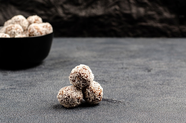 Photo boulettes d'énergie maison de dattes, d'arachides, d'avoine, saupoudrées de noix de coco dans un bol noir sur un fond sombre avec copie espace