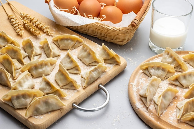 Boulettes de gyoza crues sur une planche à découper Oeufs dans un panier en osier et verre de lait Vue de dessus Fond gris