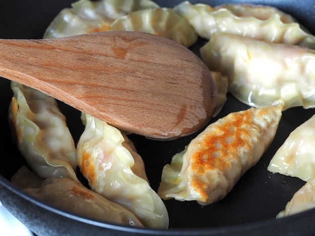 Les boulettes sont frites dans une poêle. Plat asiatique avec une variété de garnitures. Gyoza frit