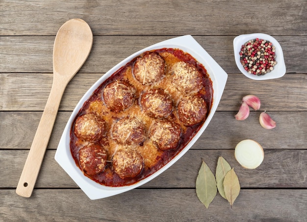 Boulettes de viande sur une assiette blanche avec sauce tomate fromage fondu et assaisonnements