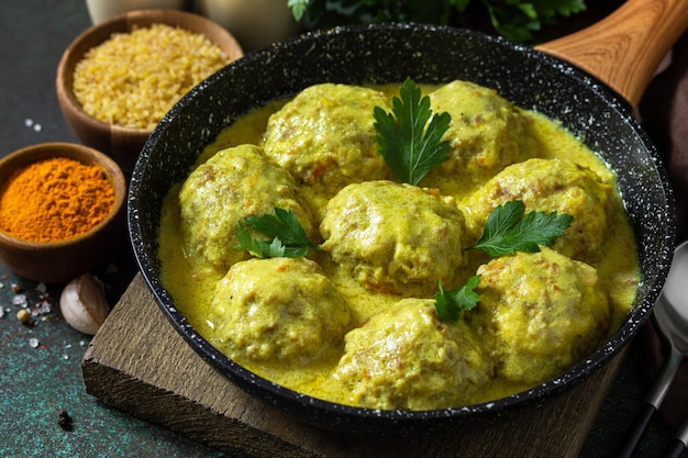 Boulettes de viande au boulgour à la crème sure et sauce au curcuma dans une poêle sur un comptoir en pierre sombre